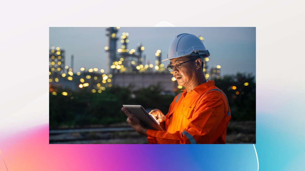 An engineer wearing a hardhat uses a digital tablet while working the night shift at petroleum oil refinery